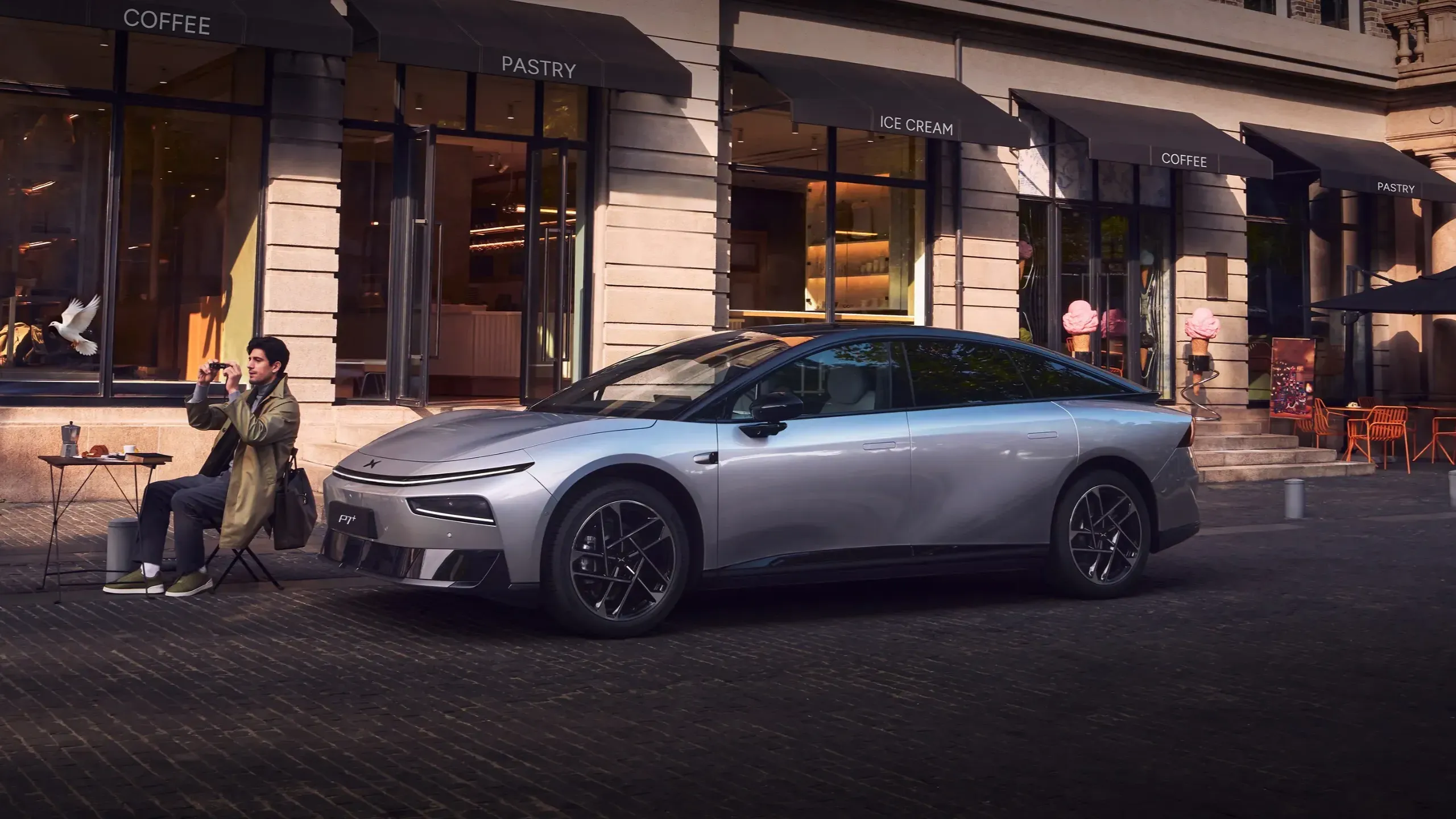 Xpeng P7+ — petmetrska fastback limuzina pred kavarno